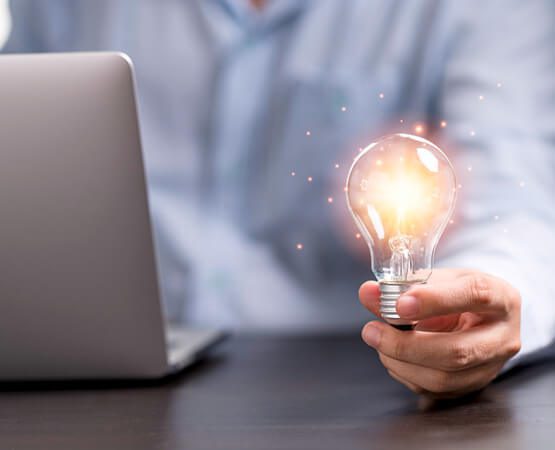 A glowing lightbulb emerging from a laptop screen, held by a hand, symbolizing a bright idea, successful innovation, and the technical solution delivered for the portal.