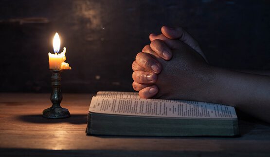 A close-up of hands resting on a keyboard in a dimly lit setting, with a microphone and a faint light source, symbolizing focused digital work, prayer, or quiet, reflective activity online.