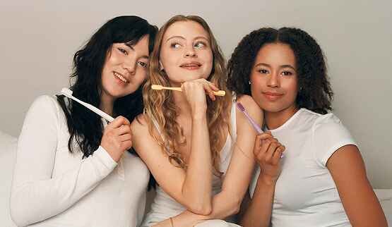 Three diverse young women smiling and posing together, symbolizing the global reach, diverse audience, and community focus of The Humble Co.'s brand.
