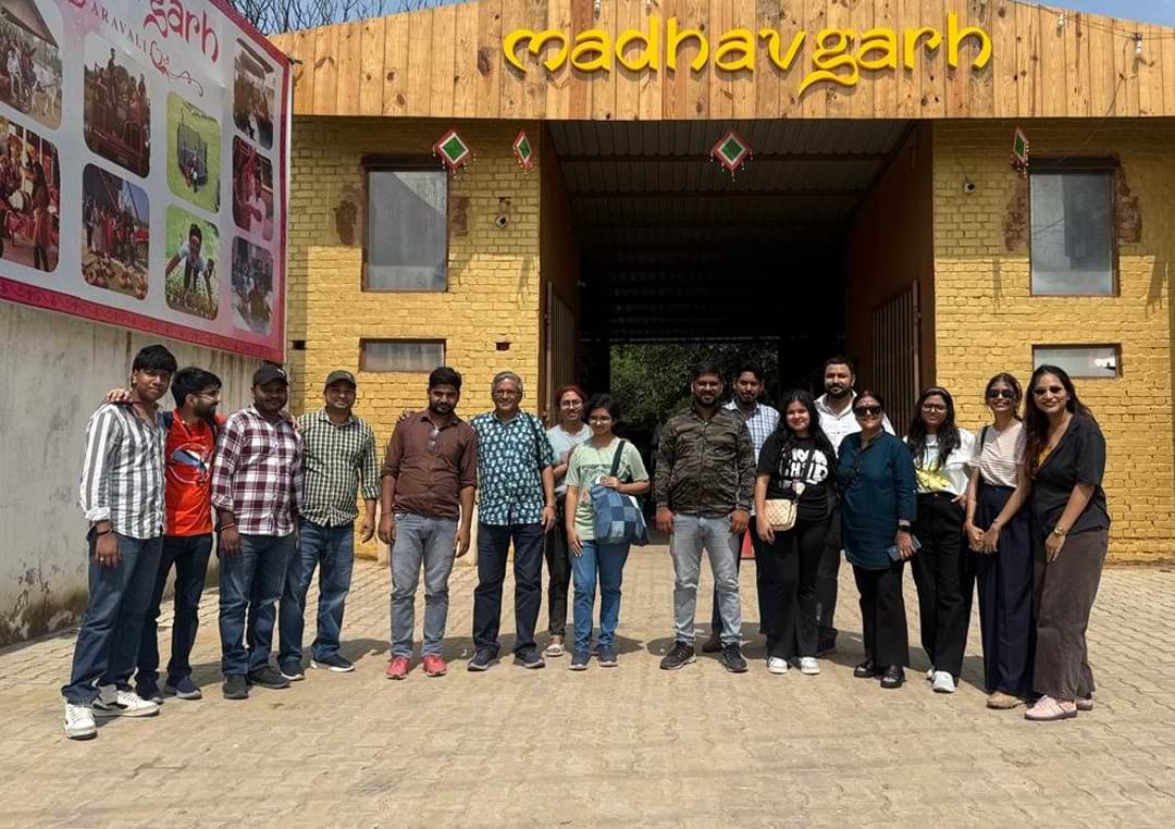 A group of Wisitech team members posing together in front of the rustic "Madhavgarh Farm" entrance sign.